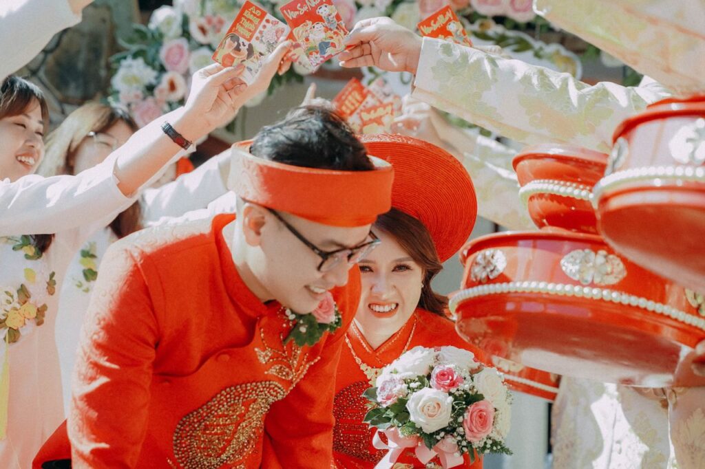 Bride and groom in traditional attire with vibrant red and white flowers during a festive Vietnamese wedding ceremony.