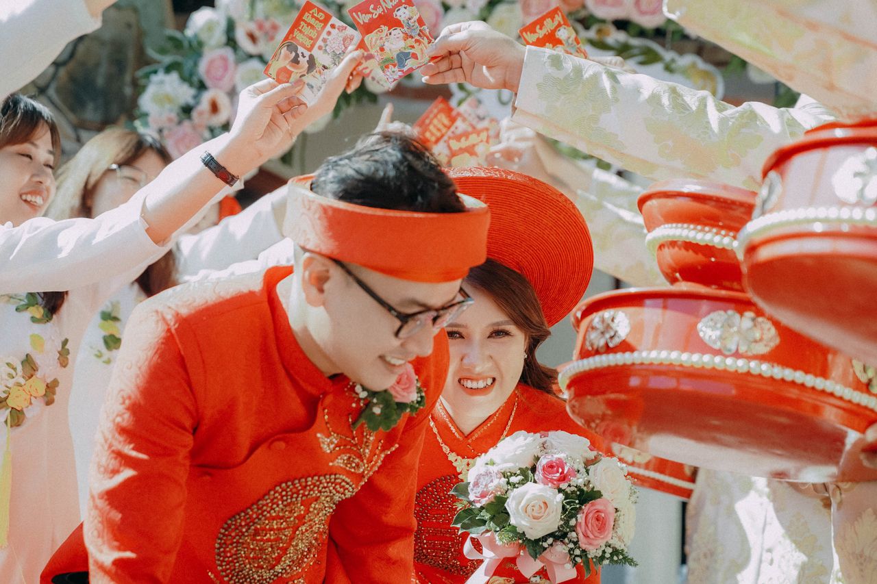 Bride and groom in traditional attire with vibrant red and white flowers during a festive Vietnamese wedding ceremony.